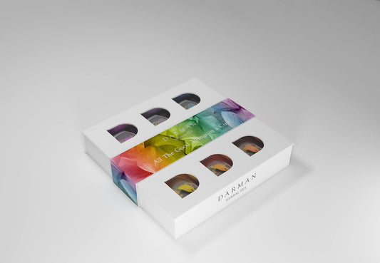 Closed white box with colorful leaf-patterned label and cut-out windows revealing inner tea sachets from Darman Specialty Herbal Tea: Organic Assortment of Herbal Tea Bags.