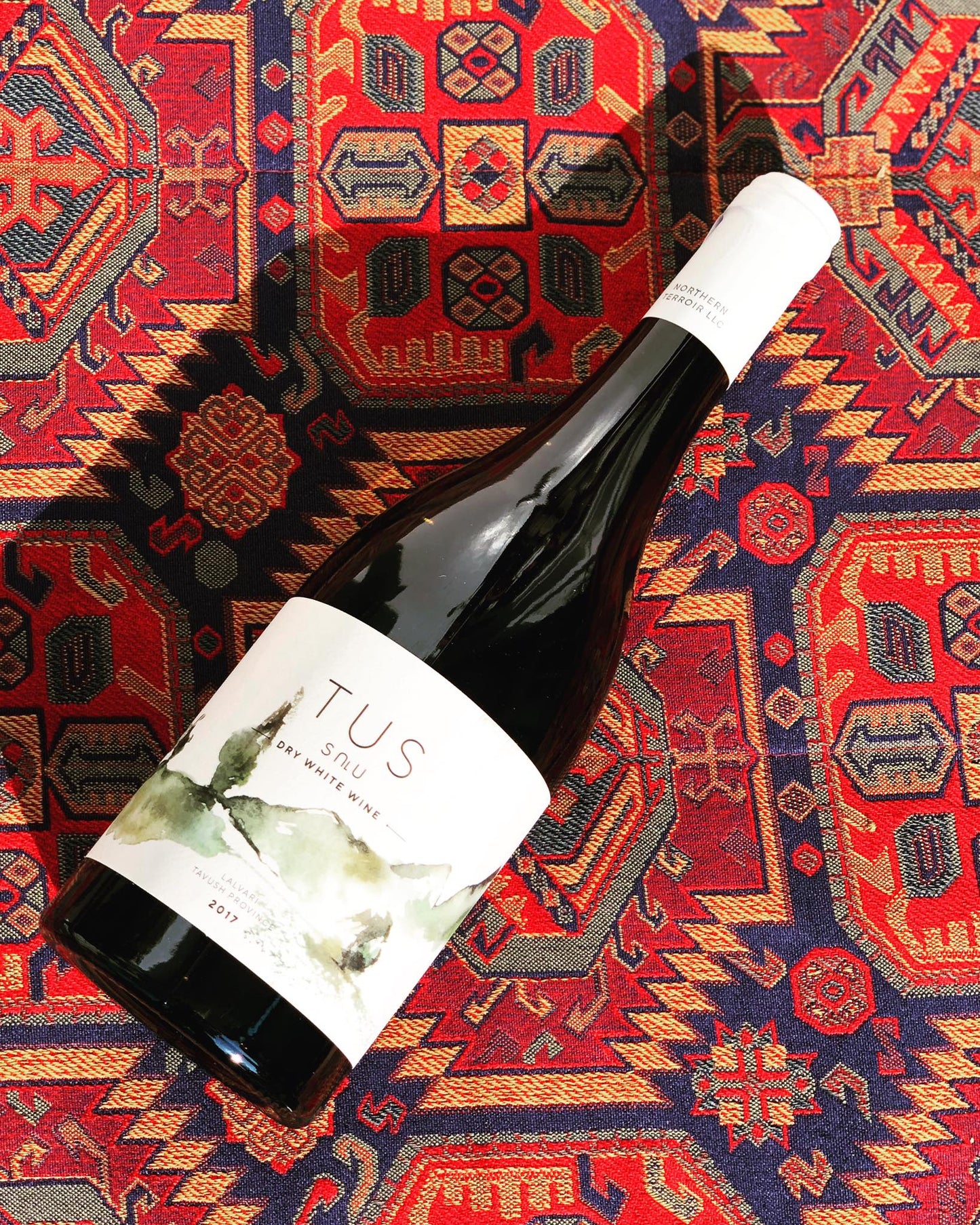 TUS Dry White Wine 2017 bottle resting on a richly patterned traditional Armenian rug, showcasing the label and white capsule.