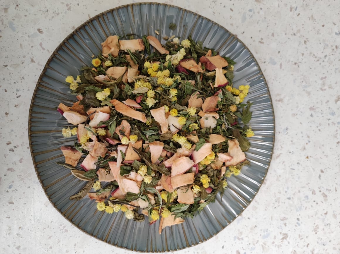 Loose herbal tea leaves of Darman N14 Fresh Zephyr blend, featuring rose petals and green herbs on a ceramic plate