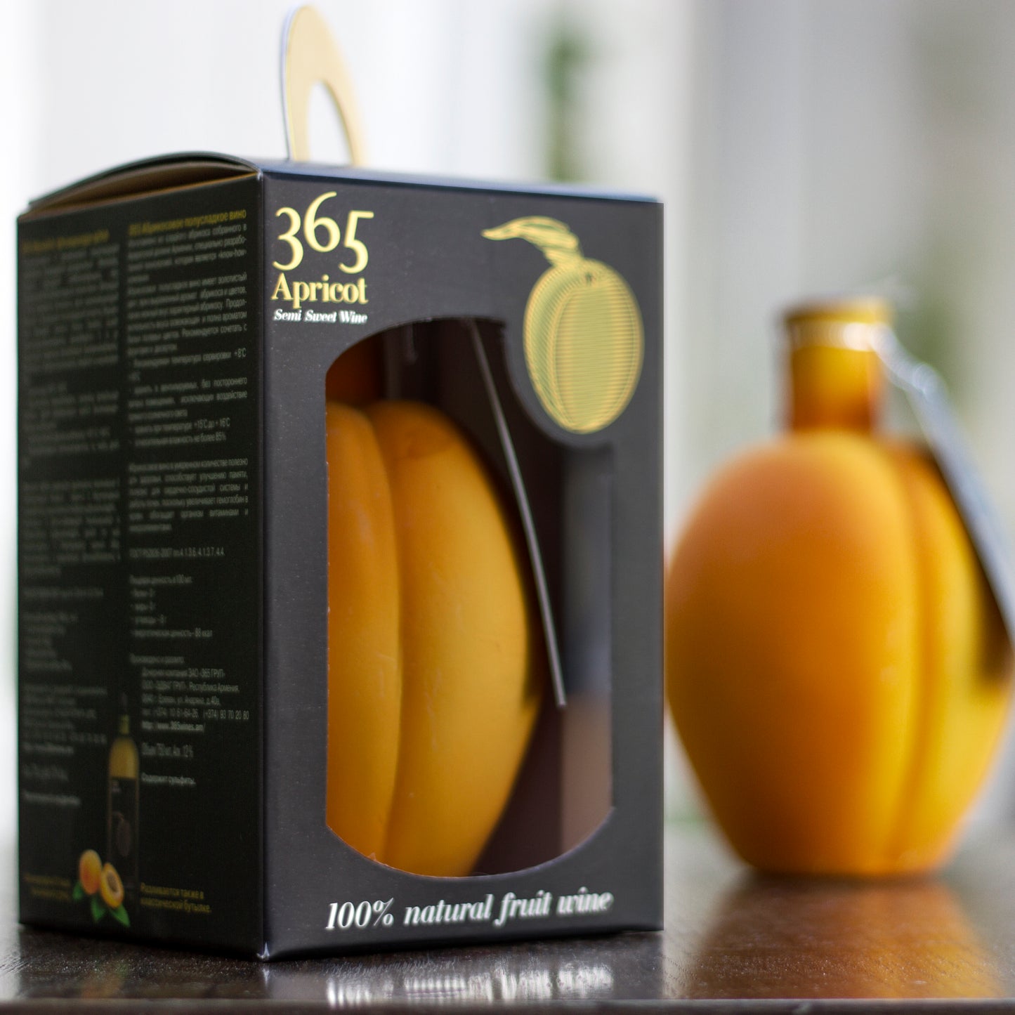 Boxed 365 Apricot Semi-Sweet Wine souvenir bottle with gold fruit label, alongside an unboxed apricot-shaped bottle in the background.