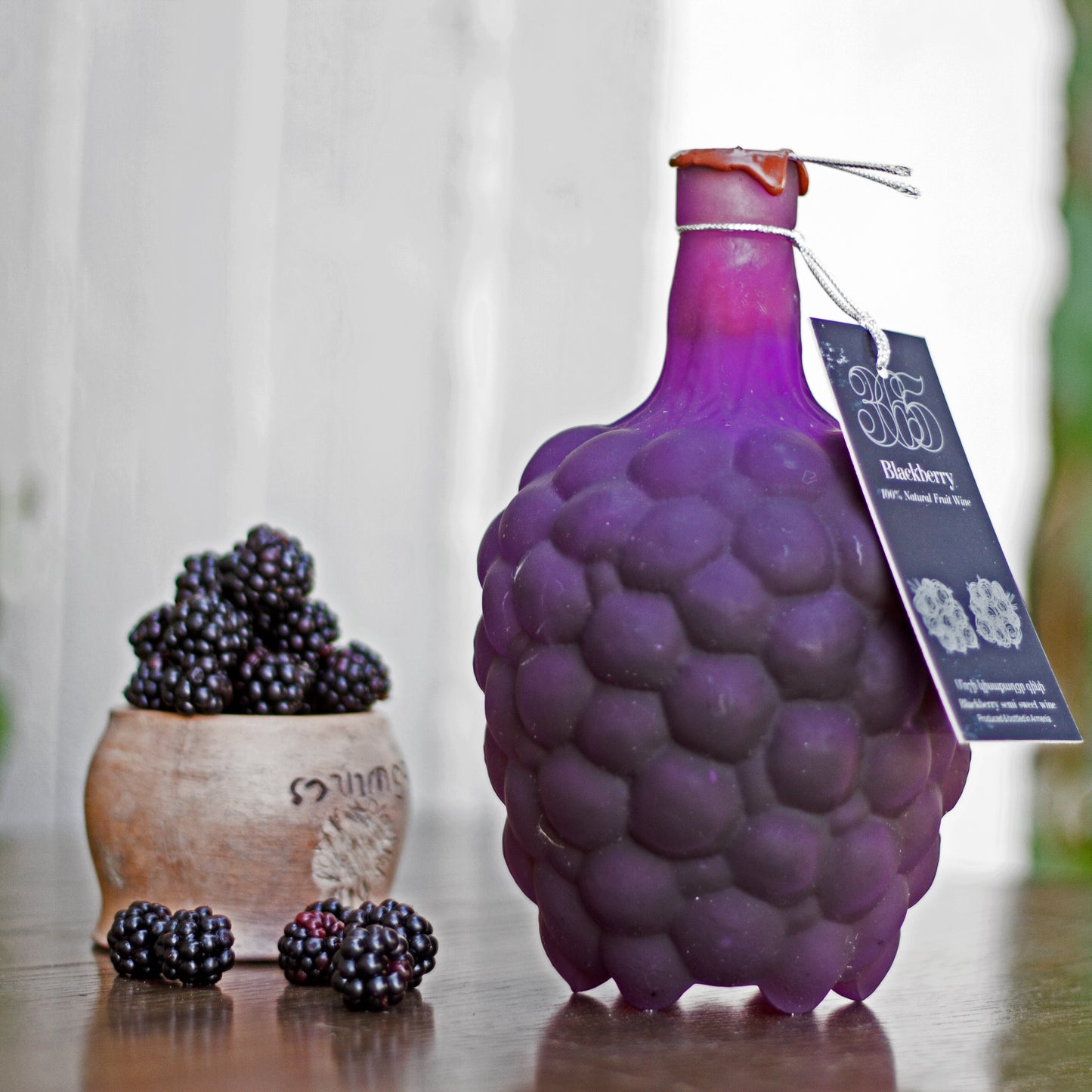 365 Blackberry Wine bottle in signature shape, displayed with fresh blackberries in a rustic ceramic cup.
