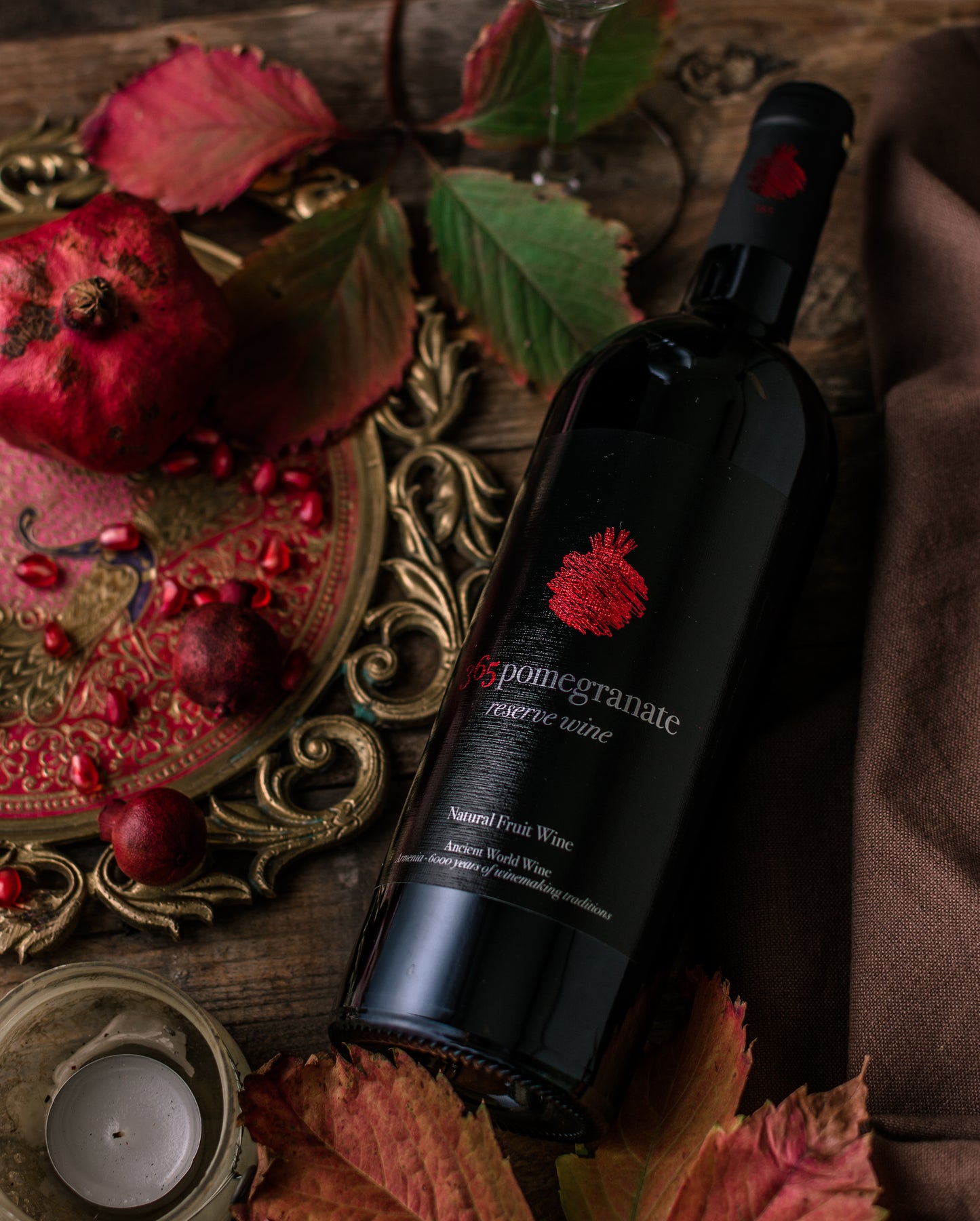 365 Pomegranate Reserve Wine bottle styled with fall leaves, pomegranates, and vintage gold tray.