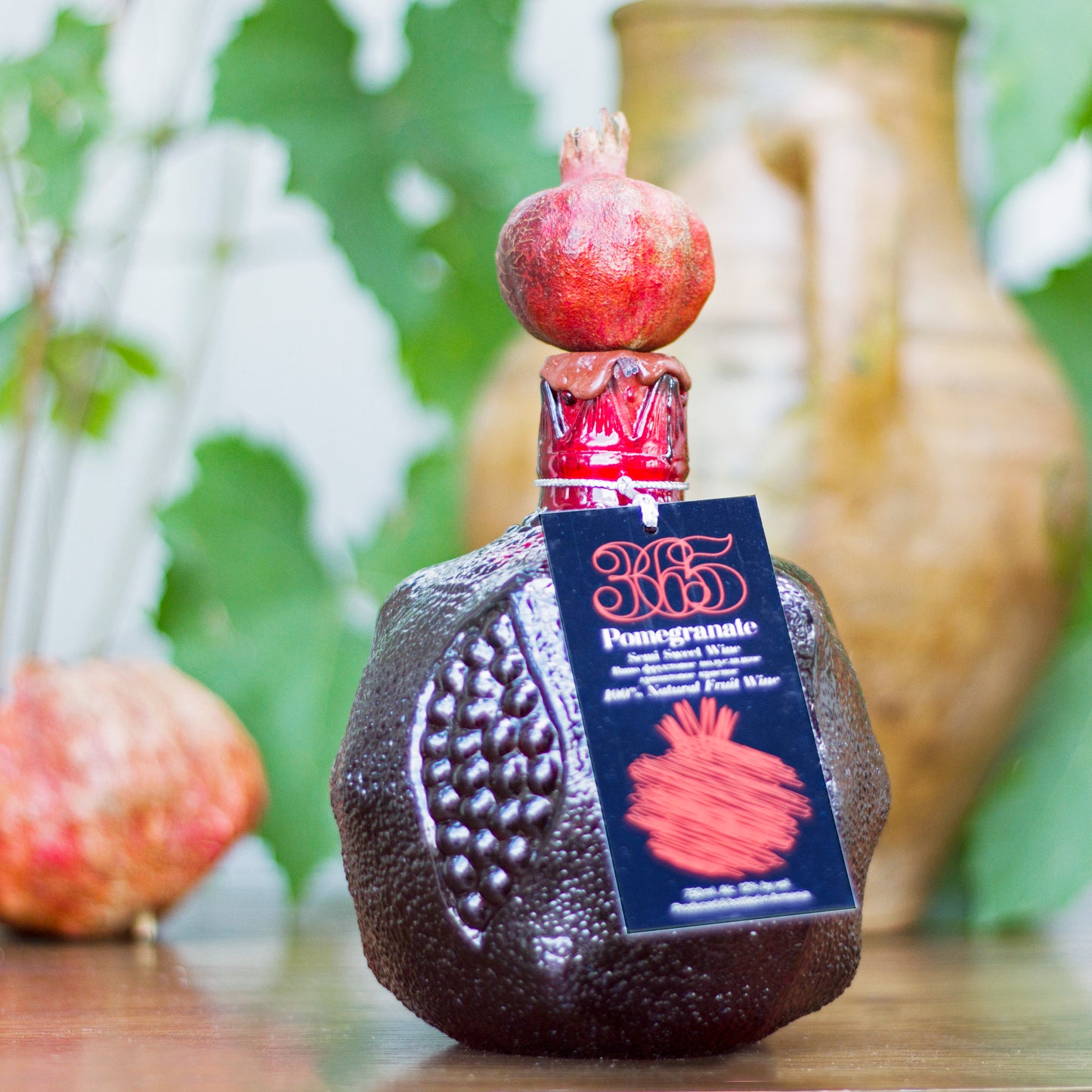souvenir bottle topped with a real pomegranate, staged with rustic Armenian pottery in the background.