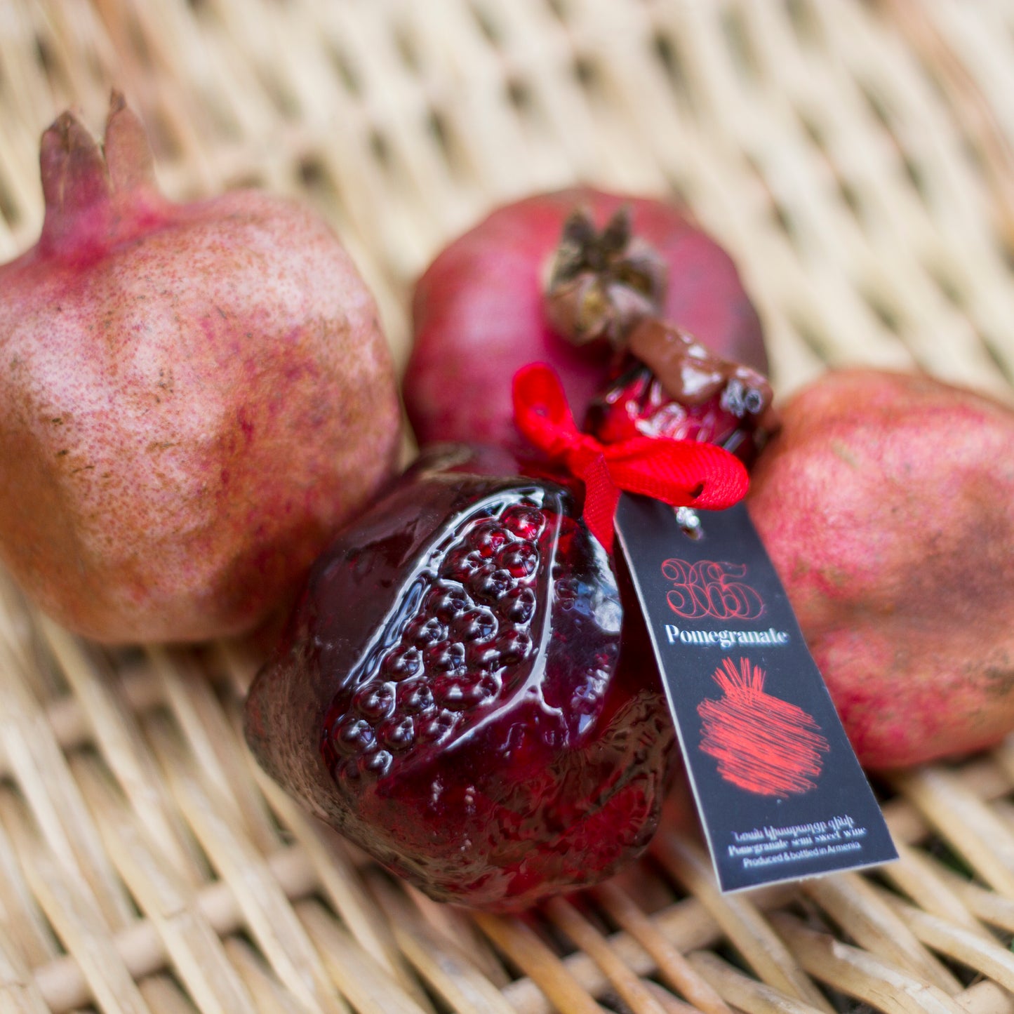 glass bottle shaped like a pomegranate with a red ribbon, placed in a wicker basket.