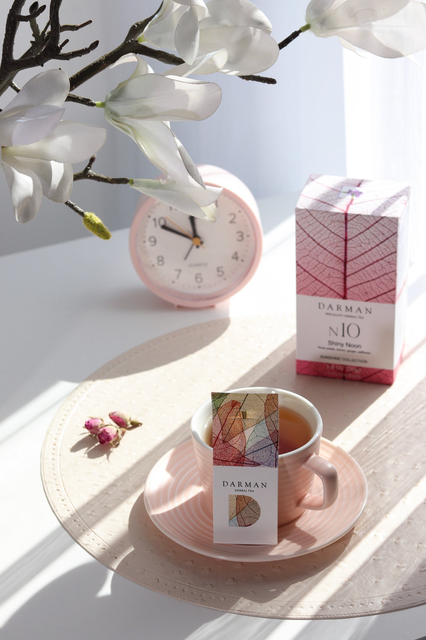 Darman N10 Shiny Noon tea box with matching teacup and clock on a sunlit table beside white flowers