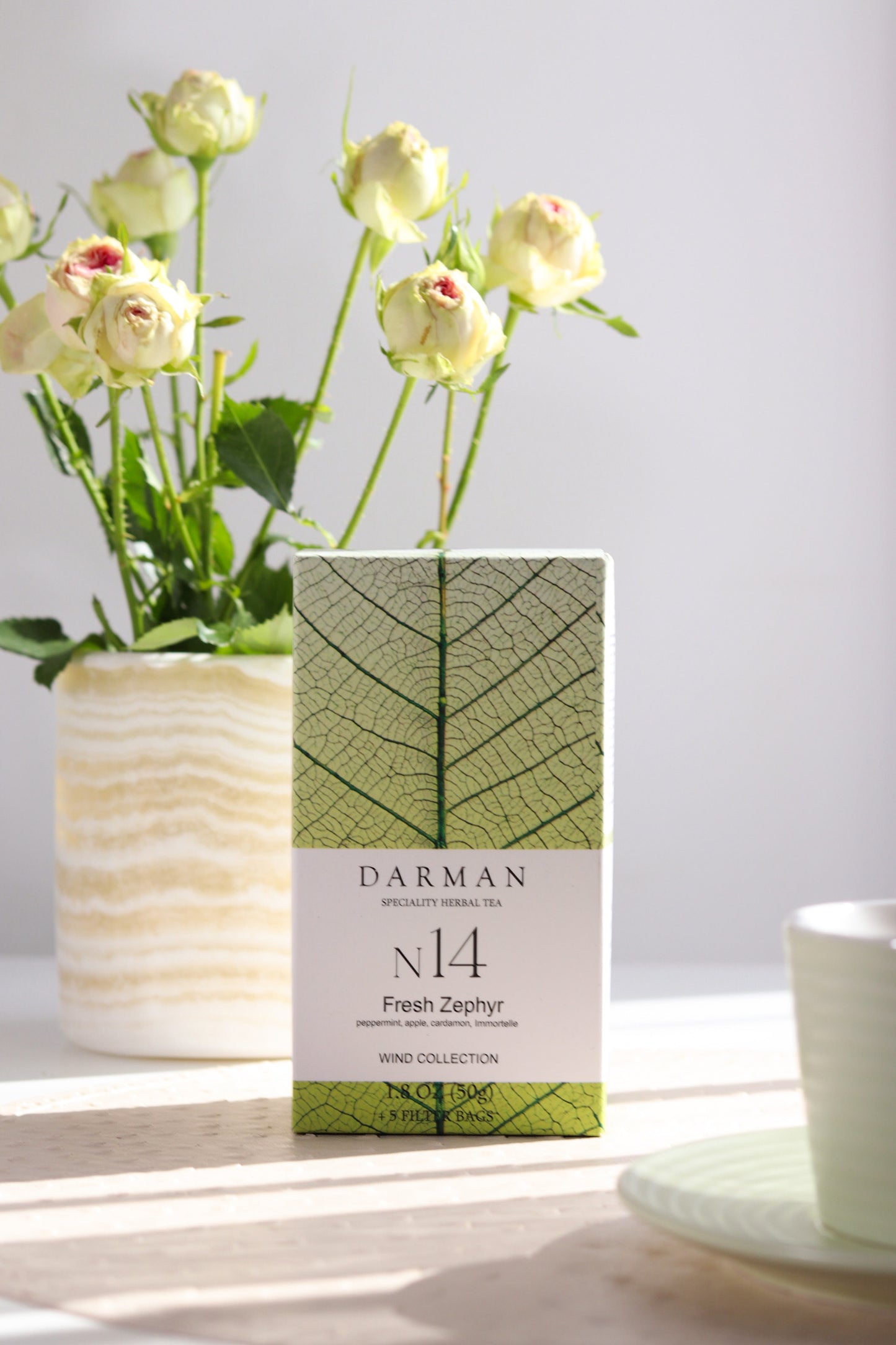 Darman N14 Fresh Zephyr tea box displayed beside a cup and flowers on a light-filled table