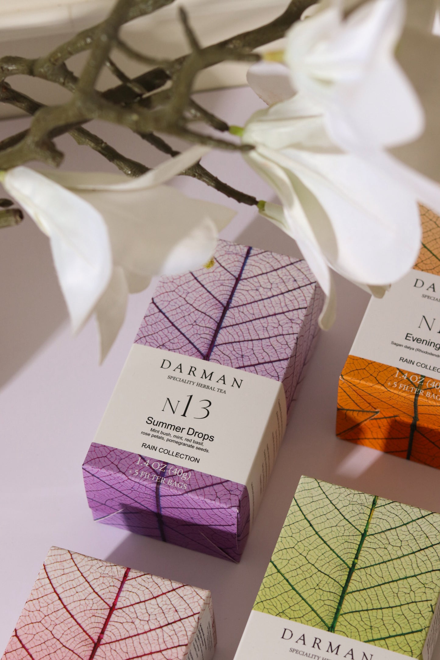 Darman N13 Summer Drops tea box displayed with other Darman teas and white flowers in a soft natural setting