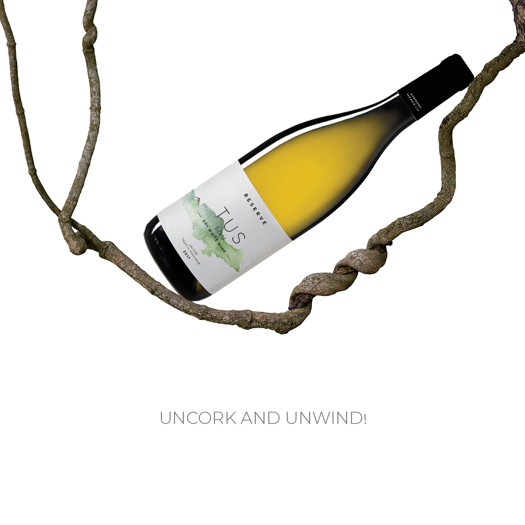 TUS Reserve Dry White Wine bottle suspended in mid-air between twisted grapevine branches with the tagline "Uncork and Unwind!" on a white background.