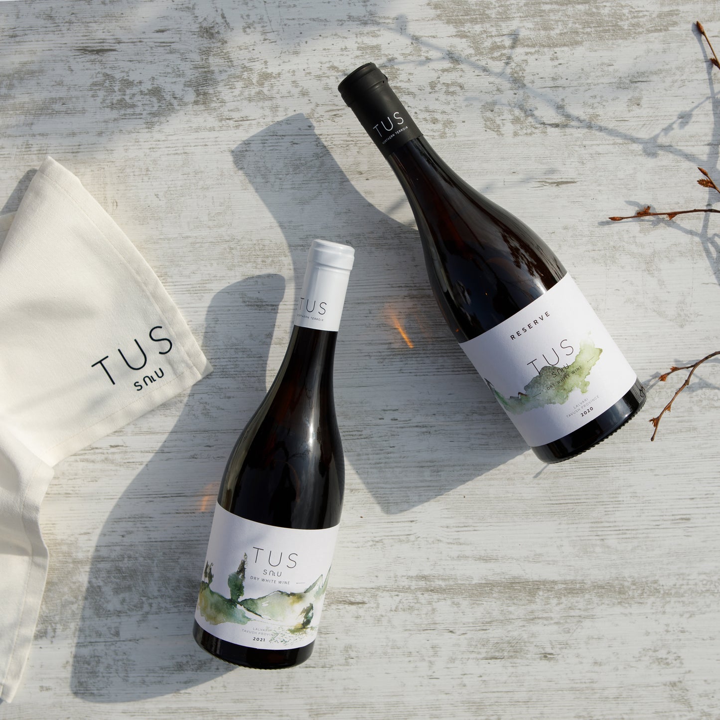 TUS and TUS Reserve Dry White Wines laid flat on a textured wooden surface beside a branded cloth napkin, under natural light.