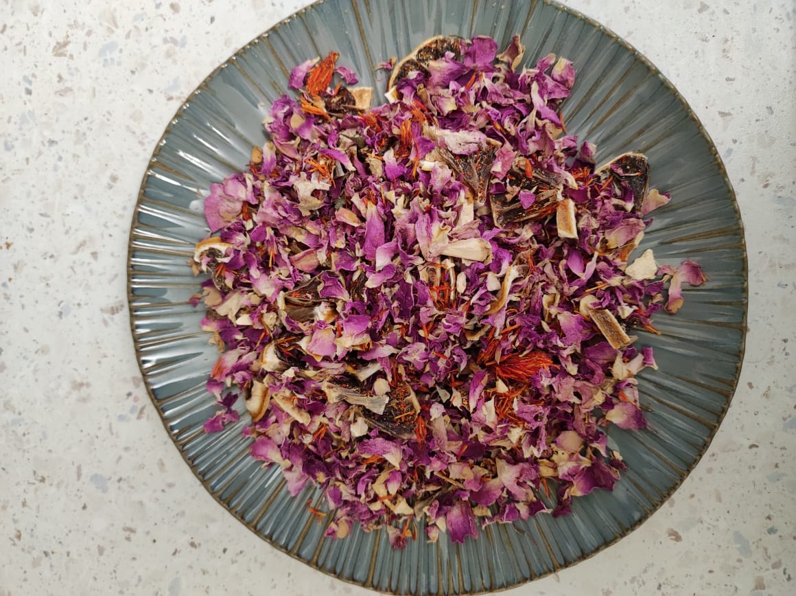 Loose herbal tea blend of Darman N10 Shiny Noon with rose petals and herbs on a ceramic plate