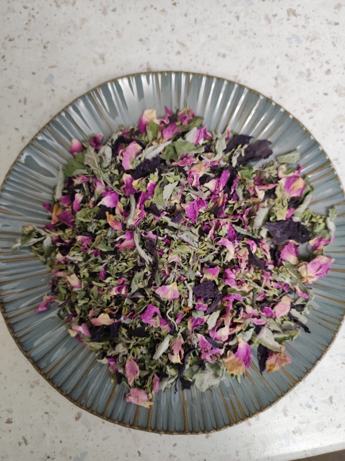 Loose herbal tea blend of Darman N13 Summer Drops with rose petals and herbs on a ceramic plate