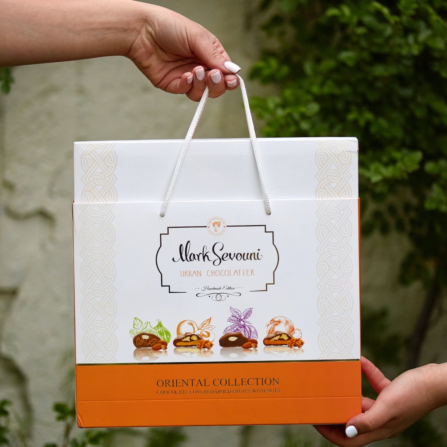 "Hand presenting Mark Sevouni Oriental Collection gift bag – luxury packaging featuring chocolate-covered dried fruits with nuts."
