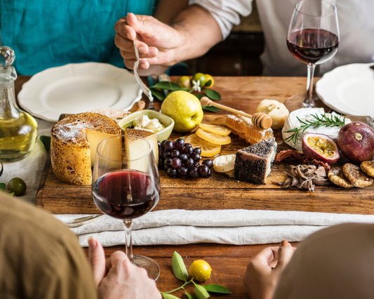 Wine and cheese pairing guide with red wine, artisanal cheeses, fresh fruits, honeycomb, figs, and charcuterie on a rustic wooden table