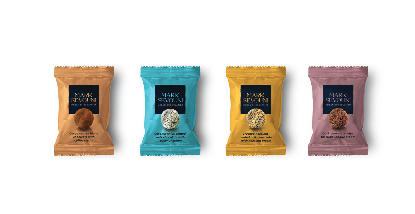 Mark Sevouni Avantgarde Chocolate Collection – four individually wrapped truffles in gold, teal, amber, and mauve packaging. Flavors include cocoa-coated blond chocolate with coffee cream, coconut chips coated milk chocolate with coconut cream, crushed hazelnut coated milk chocolate with hazelnut cream, and dark chocolate with luscious fondue cream.