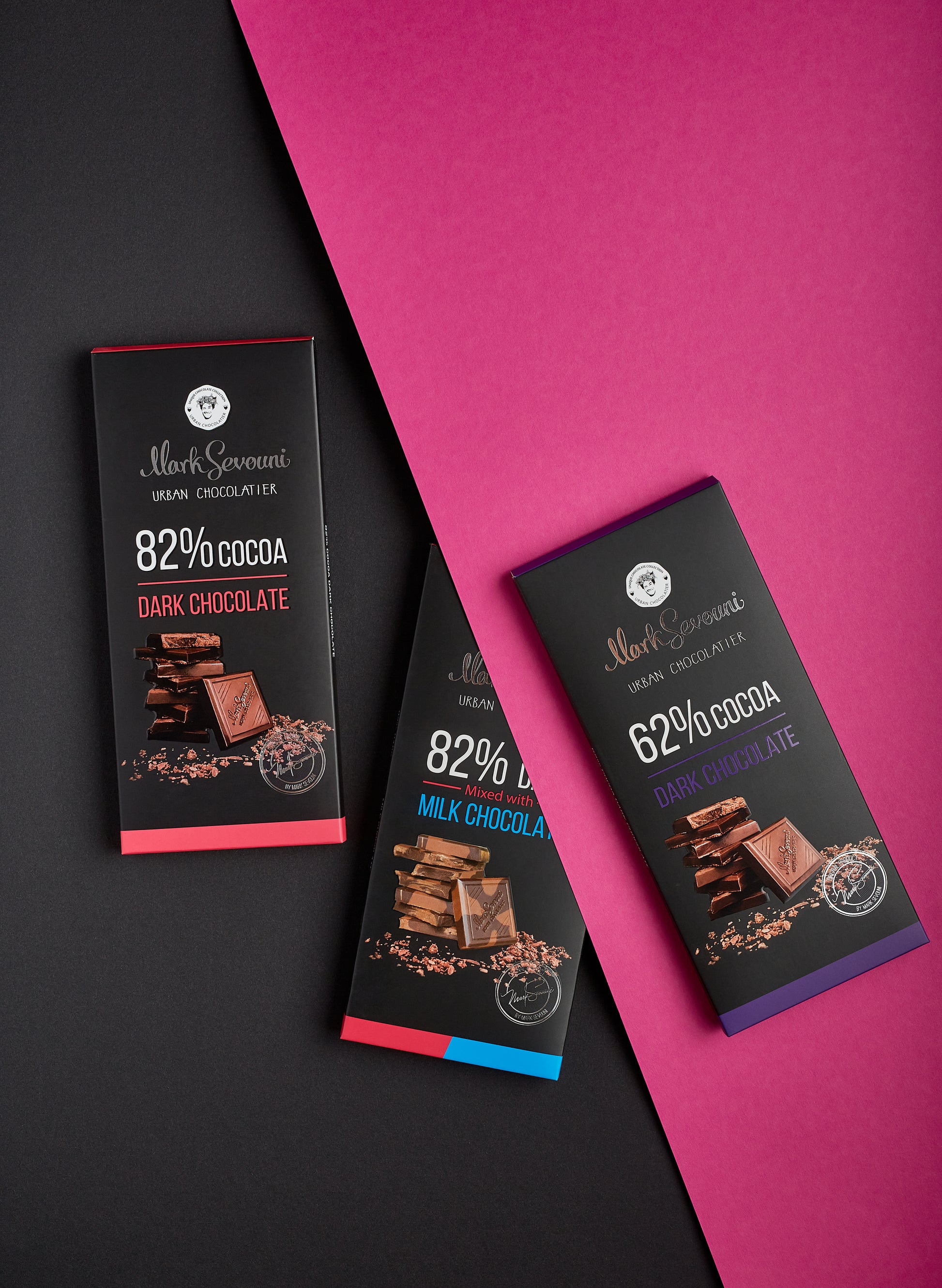 Three Mark Sevouni Urban Chocolatier dark chocolate bars arranged on a black and magenta background. Flavors shown include 82% Cocoa Dark Chocolate, 82% Dark mixed with Milk Chocolate, and 62% Cocoa Dark Chocolate.