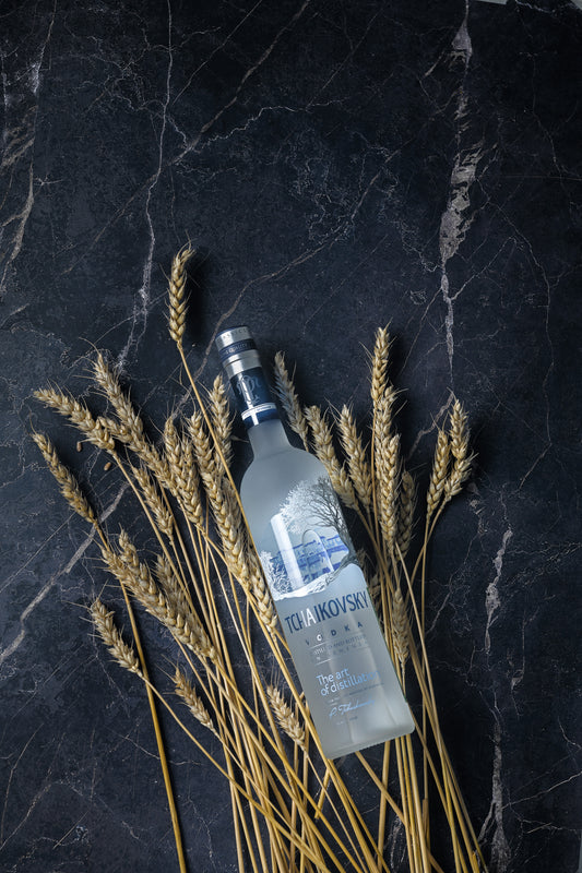 Tchaikovsky Vodka bottle surrounded by wheat on a dark marble surface, emphasizing purity and artisanal heritage.