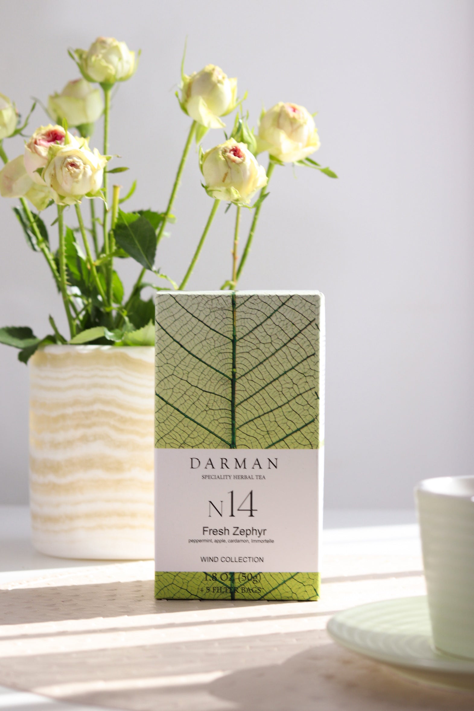 Darman N14 Fresh Zephyr tea box displayed beside a cup and flowers on a light-filled table