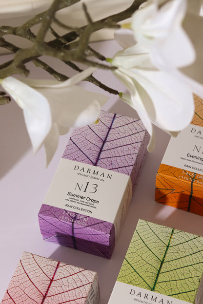 Darman N13 Summer Drops tea box displayed with other Darman teas and white flowers in a soft natural setting